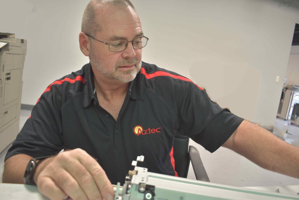 Gary Mead, Senior Service Technician, at printer and copier repair desk.