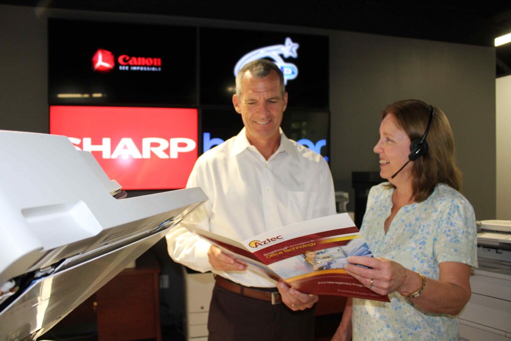 Jim Crean, Chief Operating Officer, and Danese Cox, Comptroller reviewing printer and copier equipment brochure in showroom.